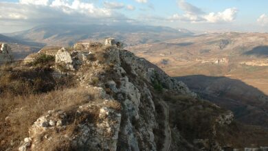 Rugged stone ruins and ramparts of Beaufort Castle sit on a rocky ridge overlooking the expansive, hilly landscape of southern Lebanon under partly cloudy skies.