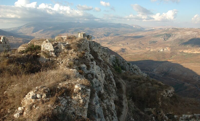 Rugged stone ruins and ramparts of Beaufort Castle sit on a rocky ridge overlooking the expansive, hilly landscape of southern Lebanon under partly cloudy skies.