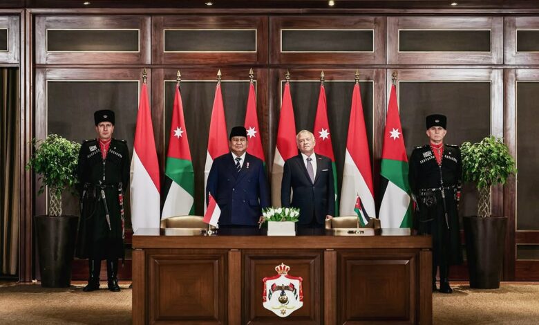 A formal signing backdrop with two officials standing before Jordanian and Indonesian flags, flanked by two Jordanian Royal Guards. A desk bearing Jordan’s national emblem and small Jordanian and Indonesian table flags is in front of them in an ornate wood-paneled government room.
