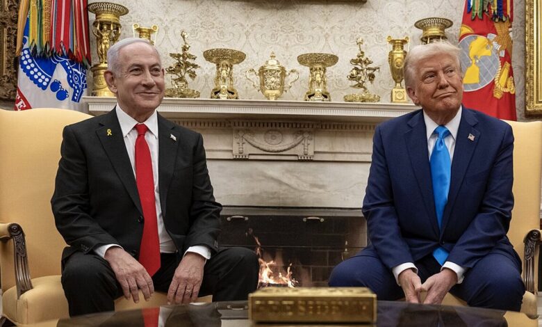 Two suited men sit side by side on armchairs in the Oval Office in front of a lit fireplace, with U.S. military flags and mantel decor visible behind them.