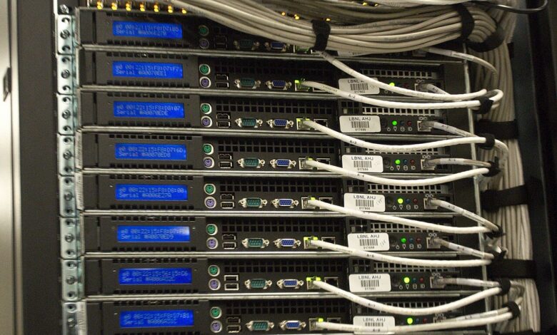 A close-up view of a tall server rack filled with multiple rack-mounted servers showing blue status screens, indicator lights, and neatly bundled white Ethernet cables in a professional data-center environment.
