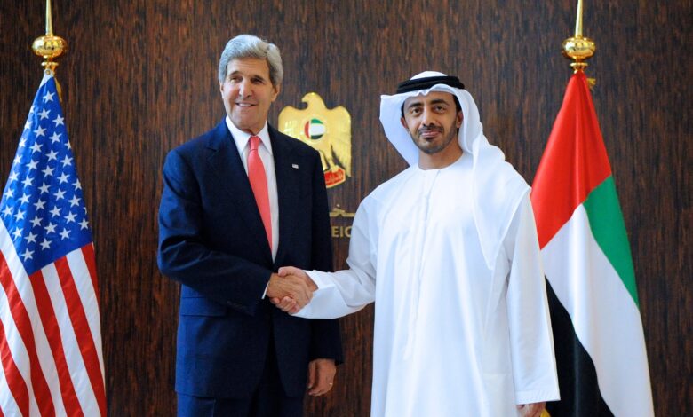 Inside the UAE Ministry of Foreign Affairs in Abu Dhabi, an Emirati official in a white kandura shakes hands with a visiting senior U.S. diplomat, standing before the ministry emblem and the UAE and U.S. flags.
