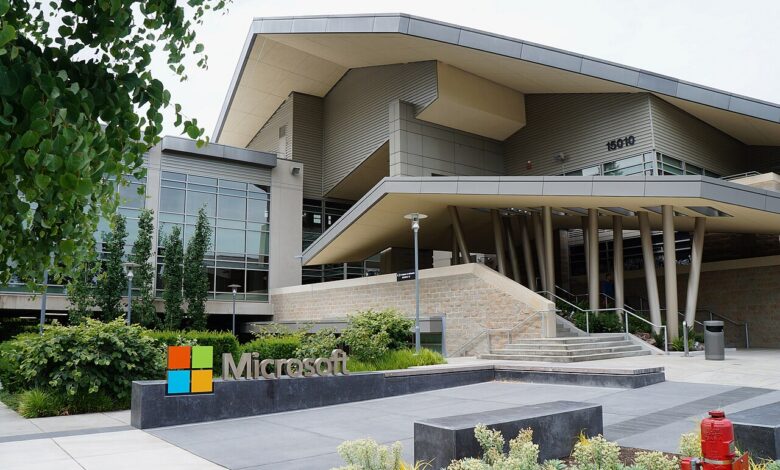 Entrance area of Microsoft Building 92 on the Redmond campus, with modern architecture and landscaping. A stone and metal sign with the Microsoft wordmark and four-square corporate logo is in the foreground.
